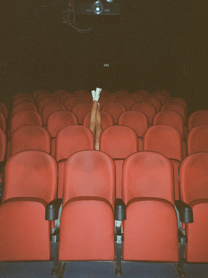 Legs raised among empty red theater seats creating a whimsical scene.